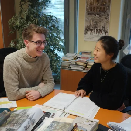 Happy tutor and Asian student in room discussing test papers on table