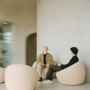 Older man and student sit in a modern beige canvas room discussing and having important conversation