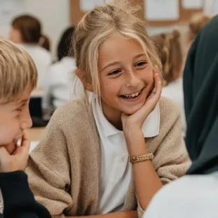 A young blonde 11 year old girl at school in a classroom sitting and talking