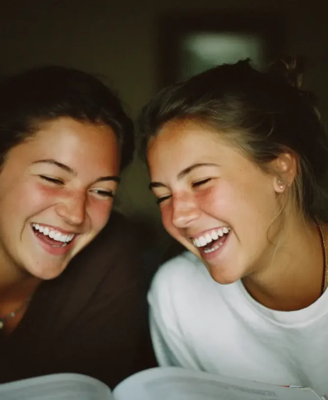 Two teenage friends laughing together over a book