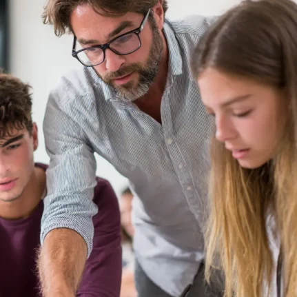 Male economics tutor teaching two teenage students in a classroom