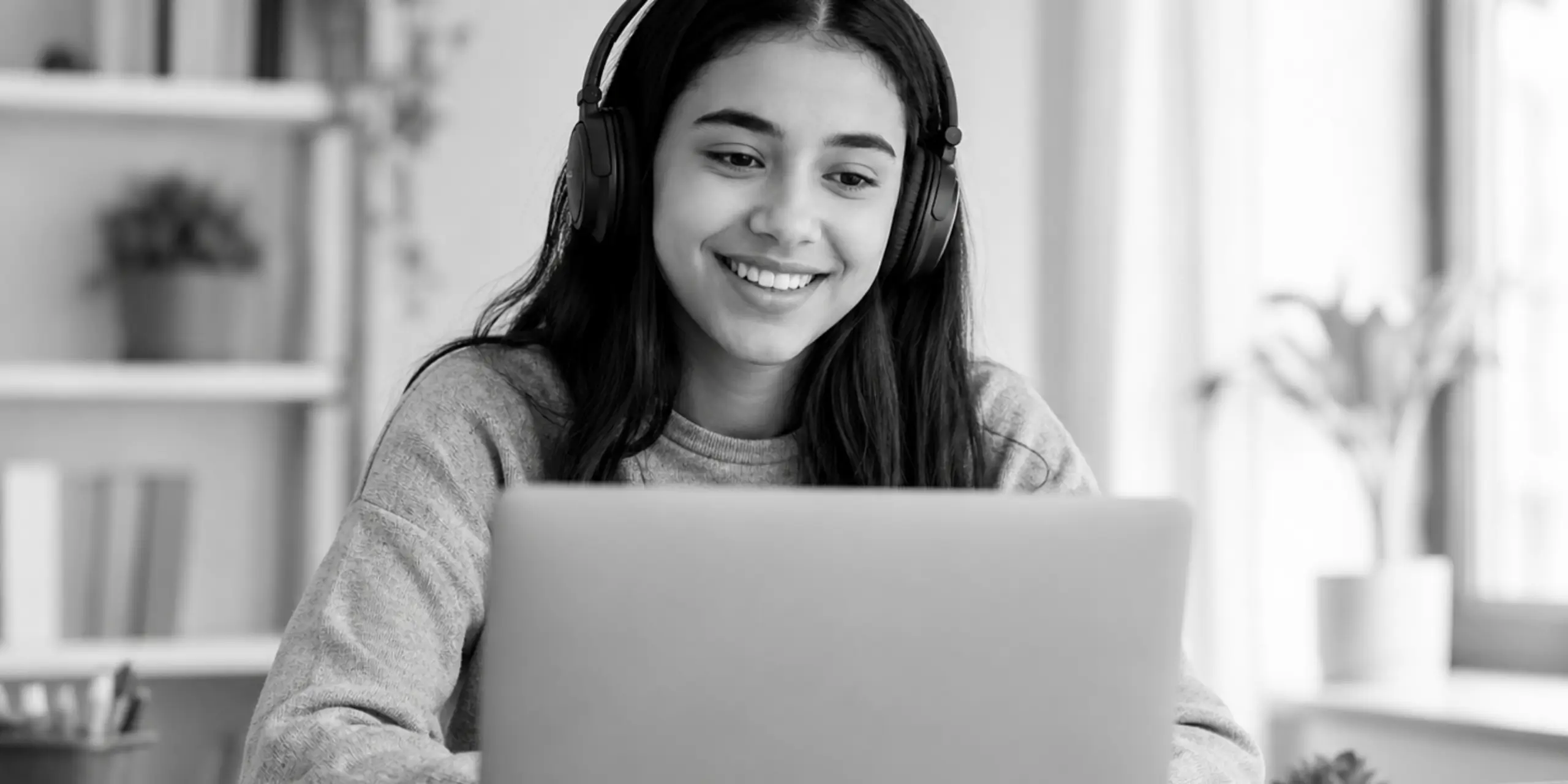 Student wearing headphones and smiling behind a laptop during an online tutoring session.