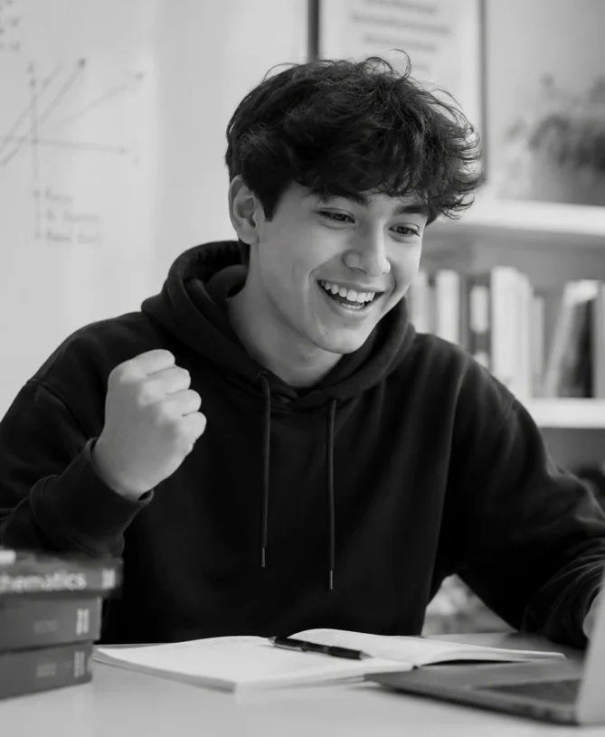 Excited student celebrating while studying online in a black-and-white academic setting.