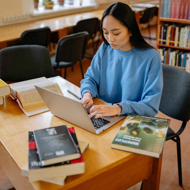 Asian student in university library studying with books on desk