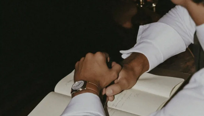 Picture of cufflinks, watch and shirt cuff on top of a notebook